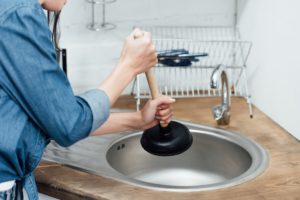 Woman Using Plunger in Kitchen